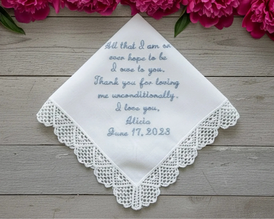 Embroidered handkerchief with personalized message on a wooden surface with pink flowers.