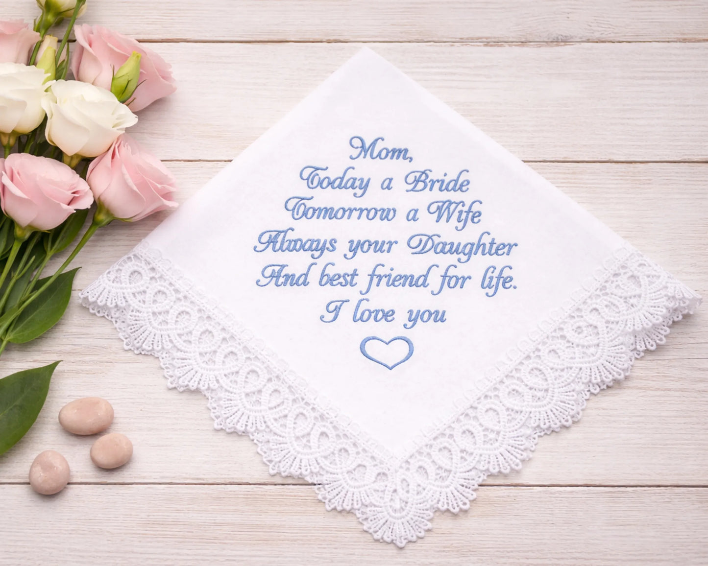 Embroidered handkerchief with a message on a wooden surface with flowers and stones.