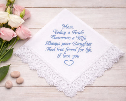 Embroidered handkerchief with a message on a wooden surface with flowers and stones.