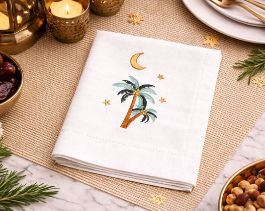 Embroidered napkin with palm tree and moon design on a decorative table setting.