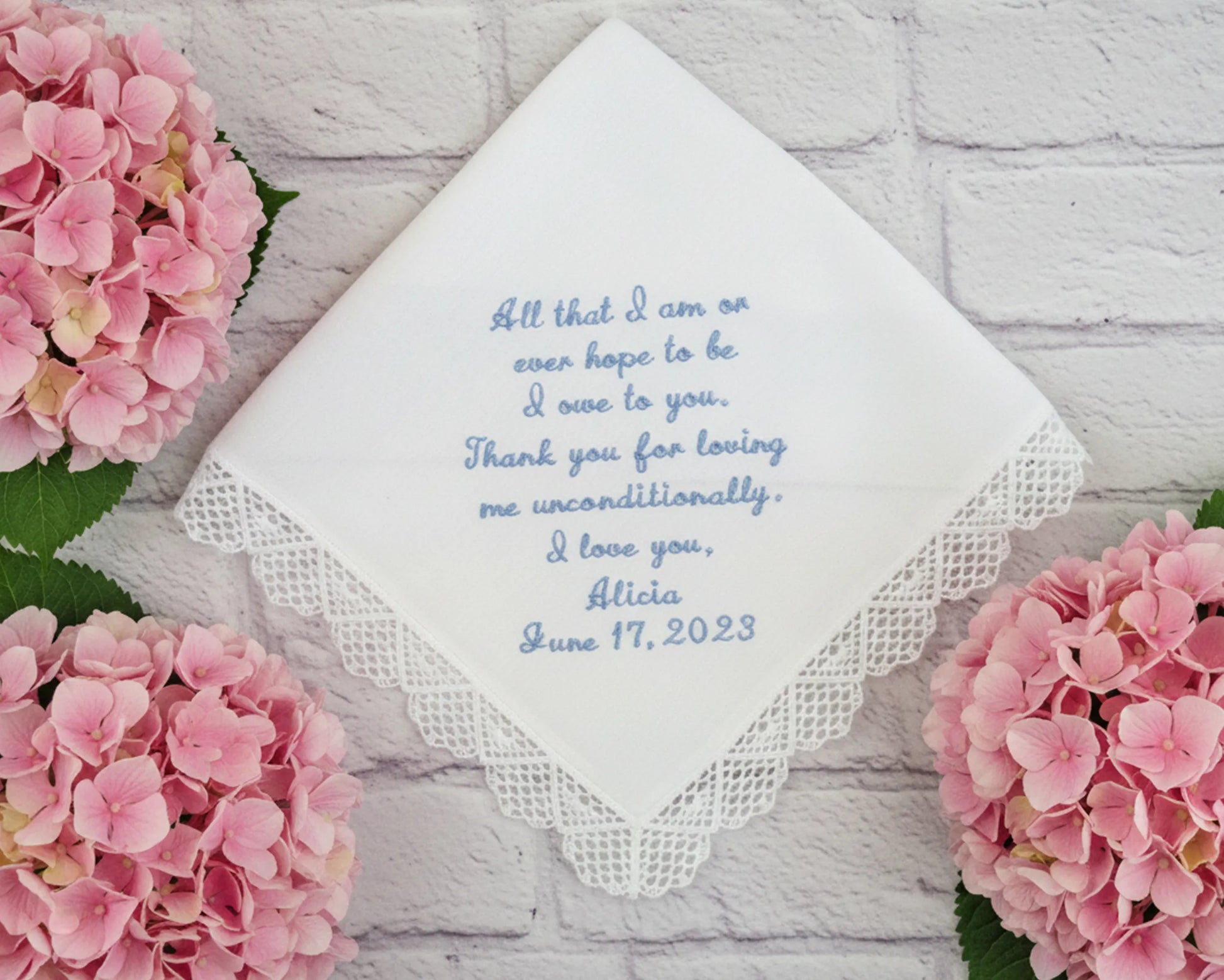 Handkerchief with embroidered message surrounded by pink flowers on a light wooden surface