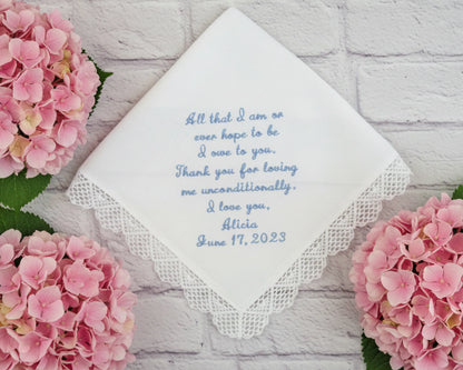 Handkerchief with embroidered message surrounded by pink flowers on a light wooden surface