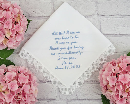 Handkerchief with embroidered message surrounded by pink flowers on a light wooden surface