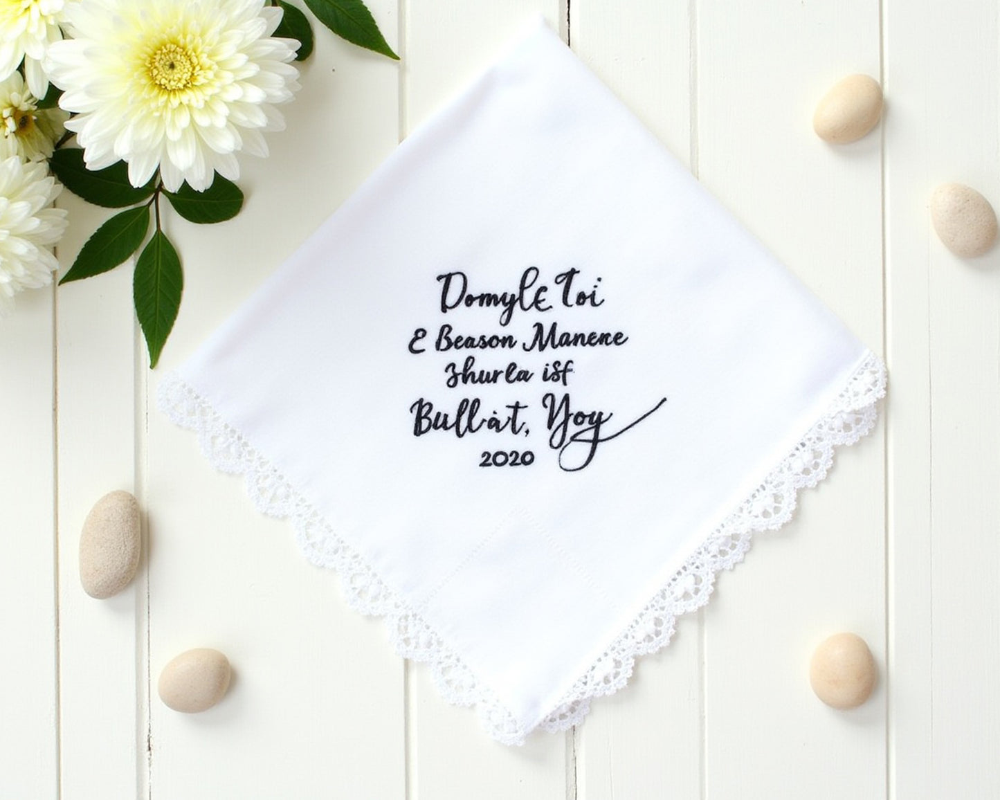 White cotton wedding handkerchief with navy blue embroidery and a wide scalloped lace border framed by white spring flowers