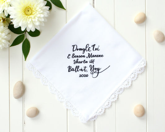 White cotton wedding handkerchief with navy blue embroidery and a wide scalloped lace border framed by white spring flowers
