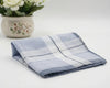 Folded blue and white checkered towel on a light surface with a decorative pot of flowers.