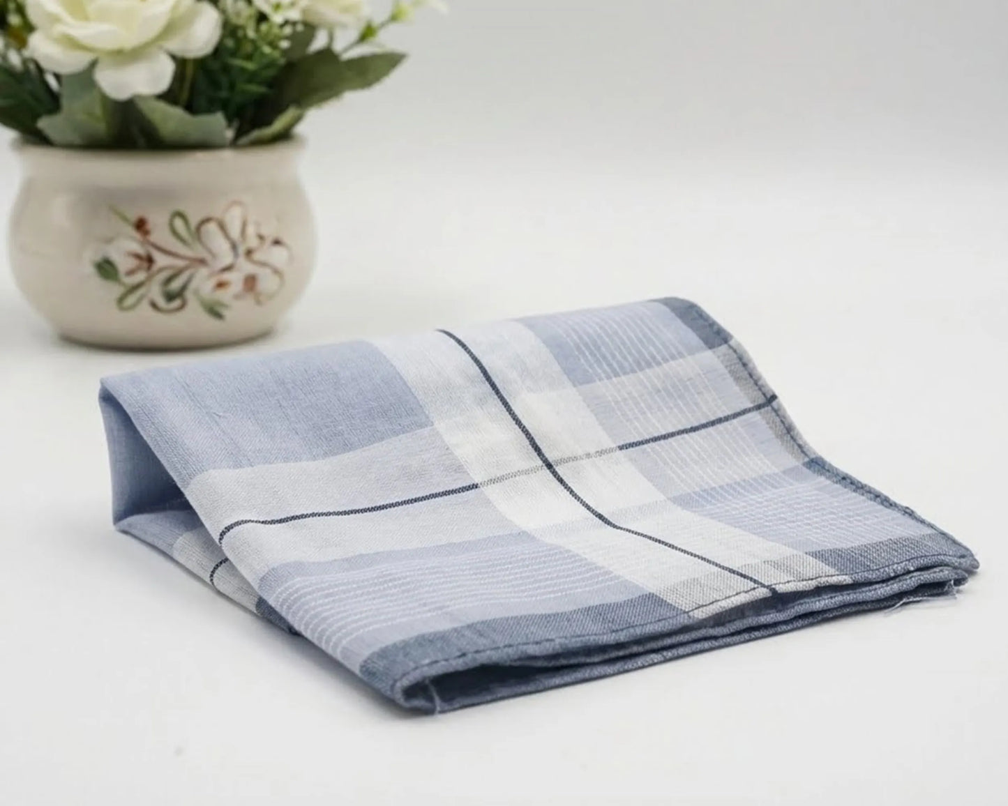 Folded blue and white checkered towel on a light surface with a decorative pot of flowers.
