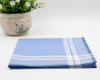Folded blue and white checkered towel on a white surface with a potted plant in the background.