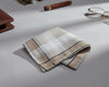 Folded checkered fabric on a light gray surface with a pen and glasses in the background.