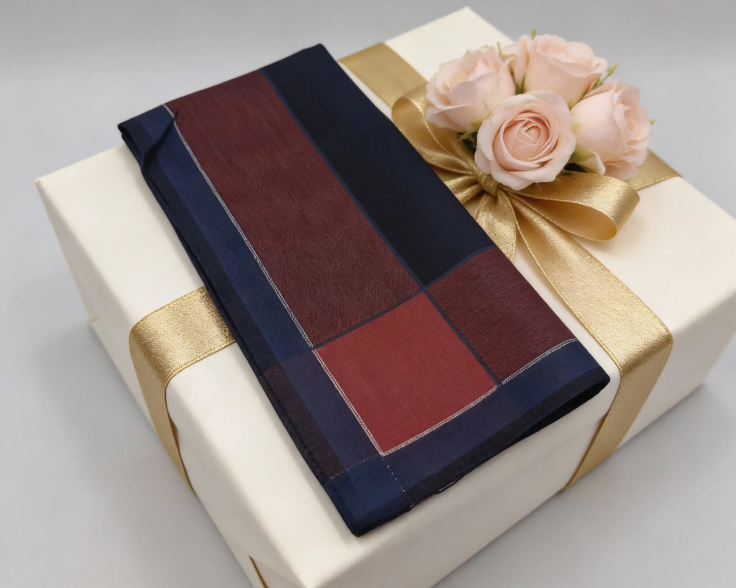 Gift box with a checkered scarf and pink roses on a light gray background