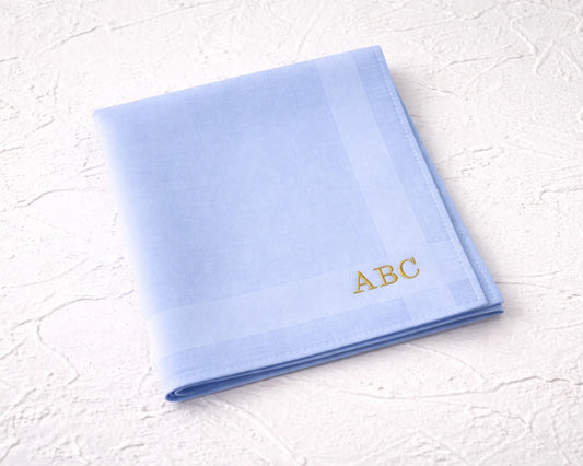 Folded light blue hanky with 'ABC' embroidery on a textured white surface