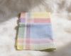Folded plaid hanky with pastel colors on a fluffy white surface
