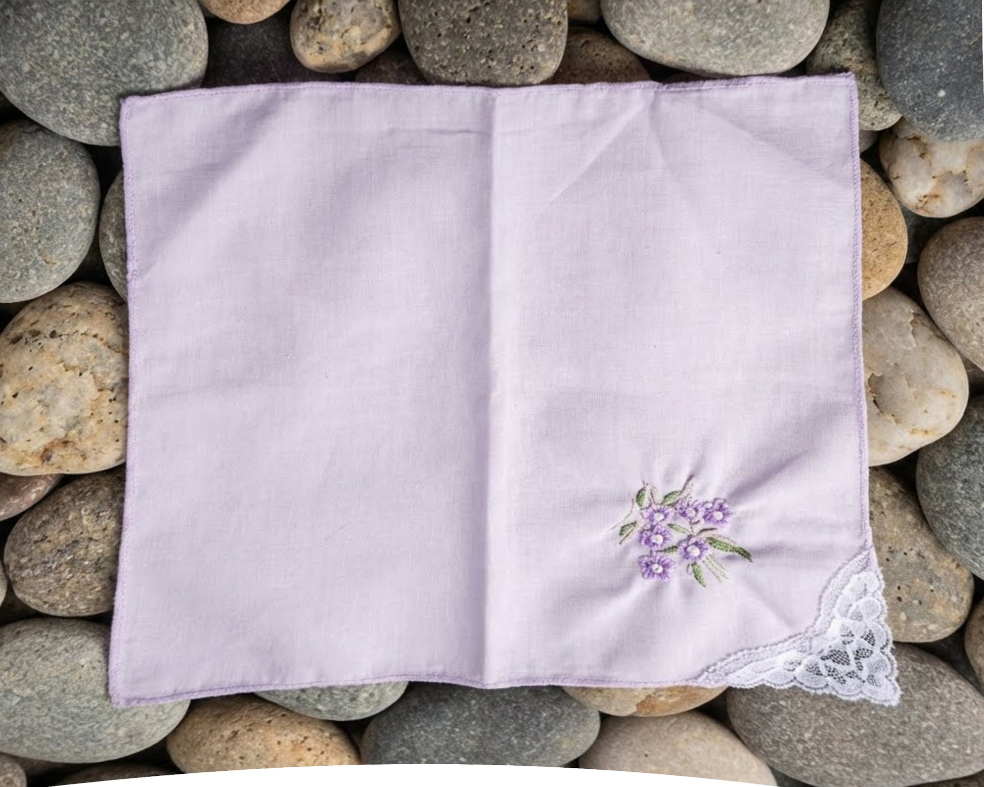 Folded purple handkerchief with floral embroidery on pebbles