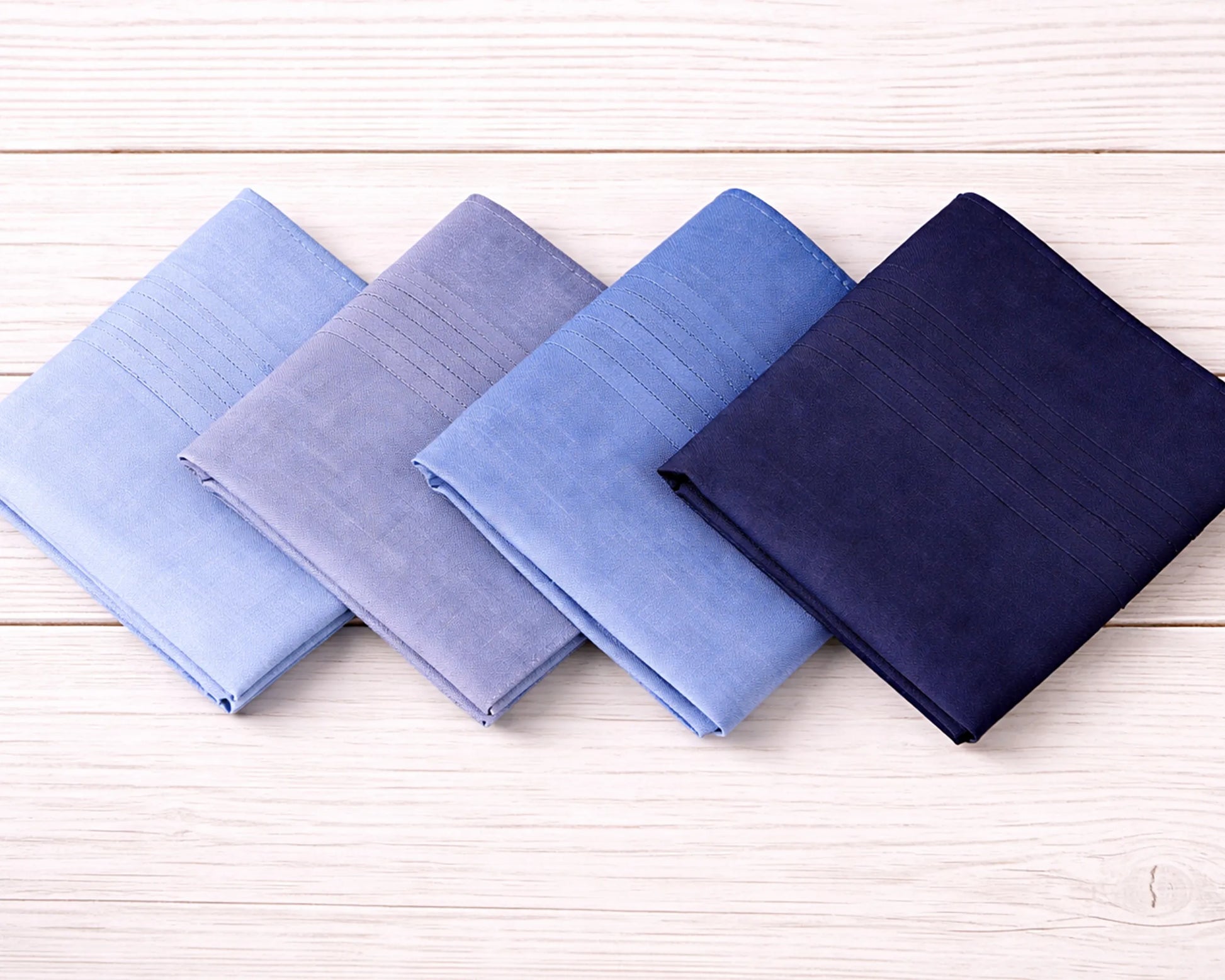 Four folded fabric swatches in blue and navy on a wooden surface