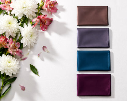Four satin fabric wallets in different colors arranged on a white surface with flowers.