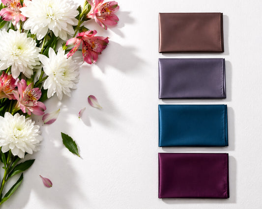 Four satin fabric wallets in different colors arranged on a white surface with flowers.