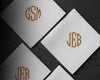 Three white cotton men's handkerchiefs with gold embroidered initials on a dark textured background