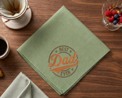 Green hanky with 'Best Dad Ever' embroidery on a wooden table with coffee and berries.