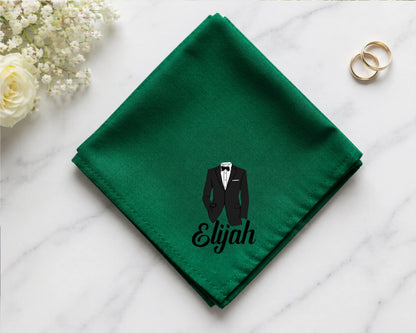 Green hanky with a tuxedo and 'Elijah' text on a white surface with flowers and rings.