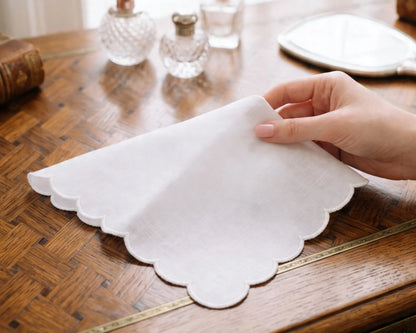 Hand holding a scalloped white hanky on a wooden table with decorative items.
