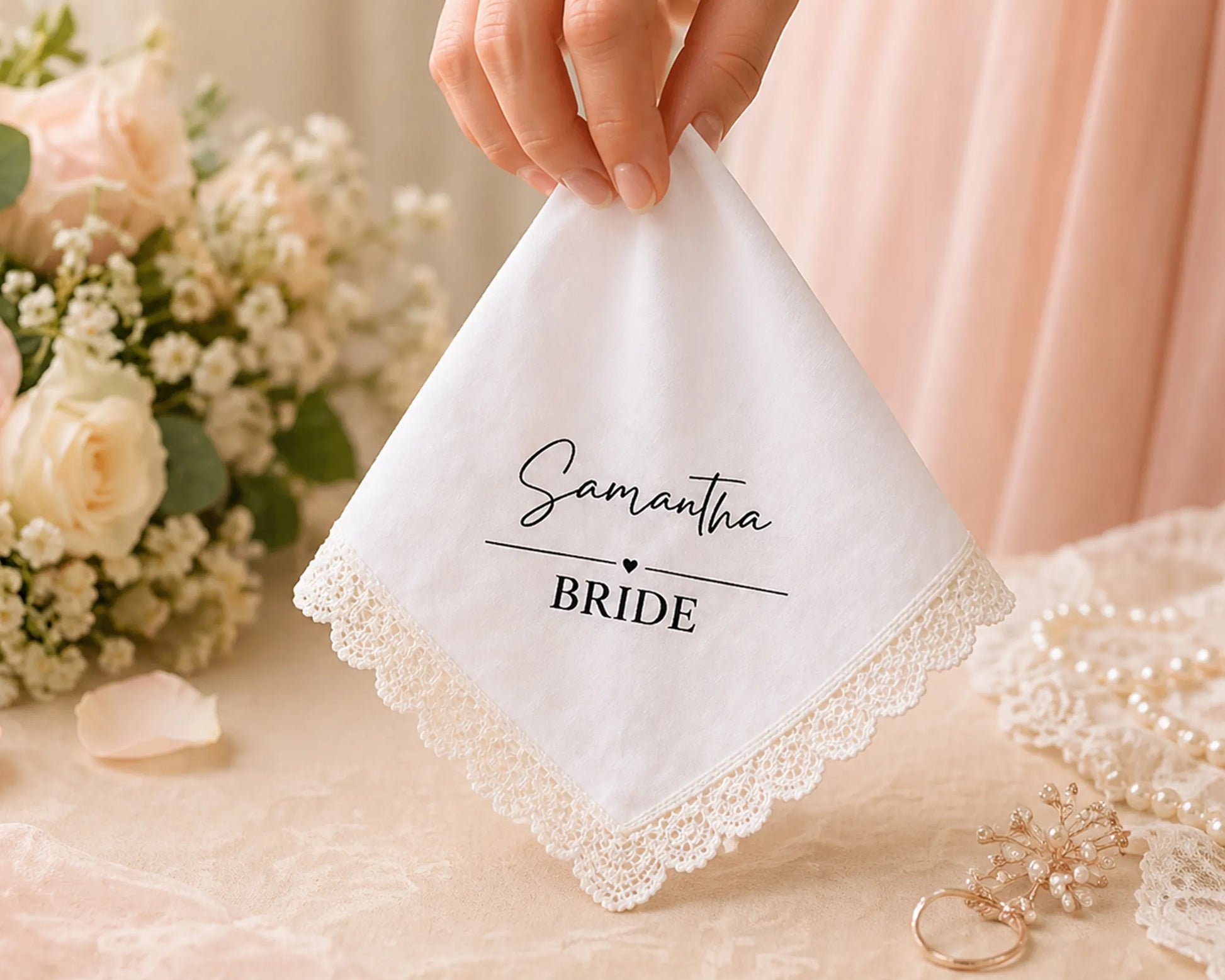 Handkerchief with 'Samantha BRIDE' text held by a hand, with flowers and jewelry in the background.