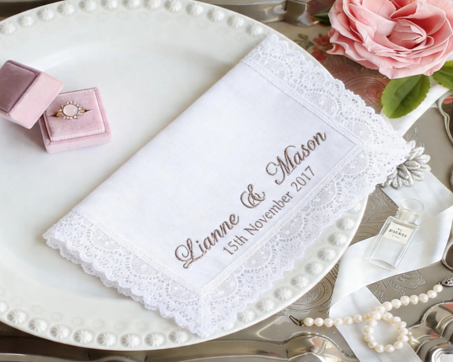 Lace handkerchief with personalized text on a table setting with jewelry and flowers.
