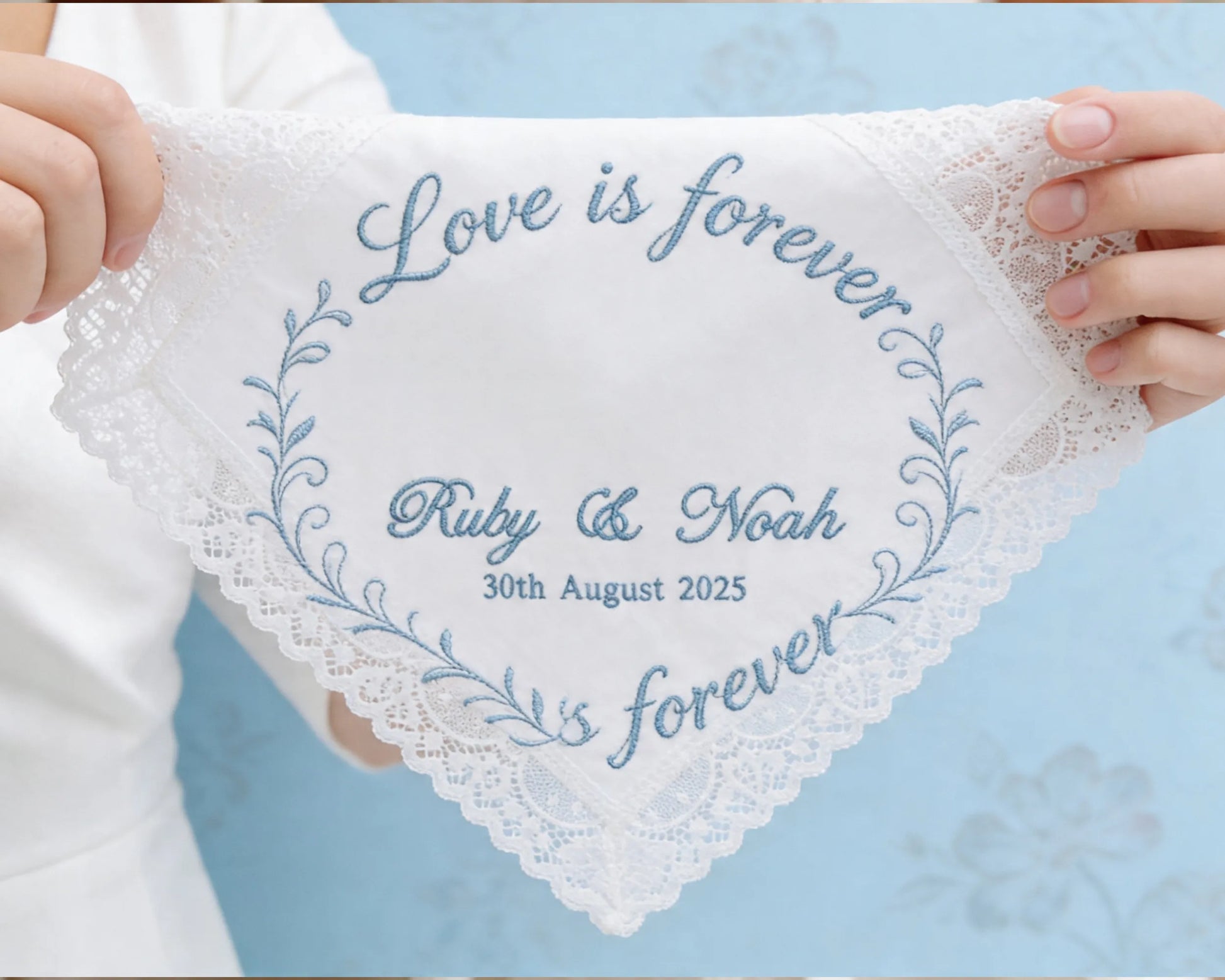 Lace handkerchief with embroidered text held by hands against a light blue background