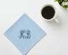 Light blue napkin with monogram 'KB' next to a cup of coffee on a white surface.