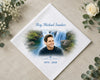 Memorial hank with a photo of a man and a waterfall, surrounded by flowers on a beige surface. 