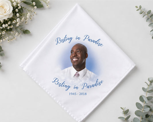 Memorial hnaky with a photo of a man and 'Resting in Paradise' text on a white background with flowers.