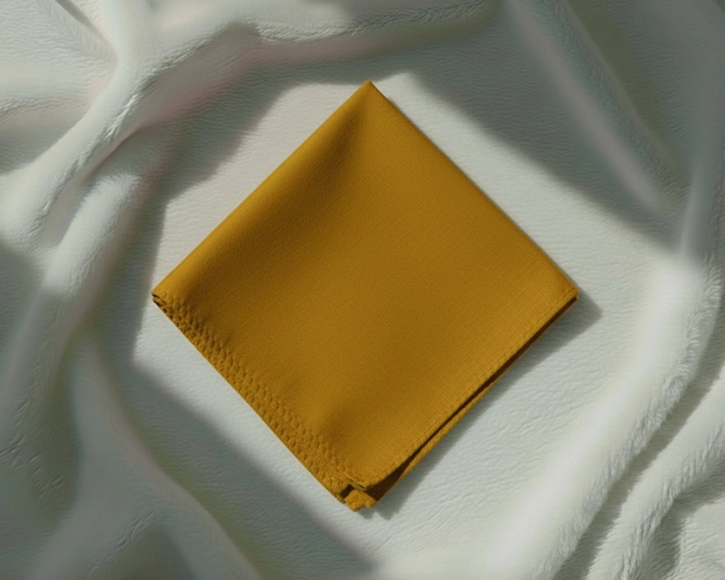 Mustard yellow fabric square on a textured white surface