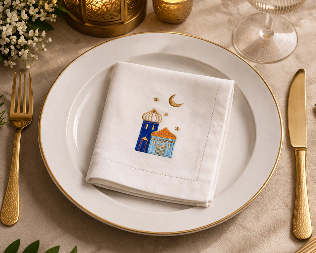 Napkin with embroidered design on a plate with gold cutlery and candles.