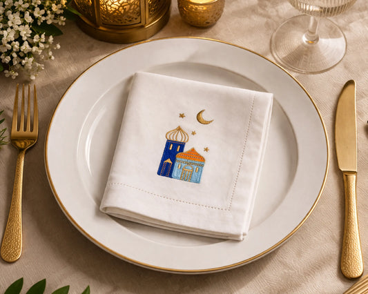 Napkin with embroidered design on a plate with gold cutlery and candles.
