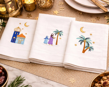 Napkins with embroidered designs of palm trees, stars, and buildings on a decorative table setting.