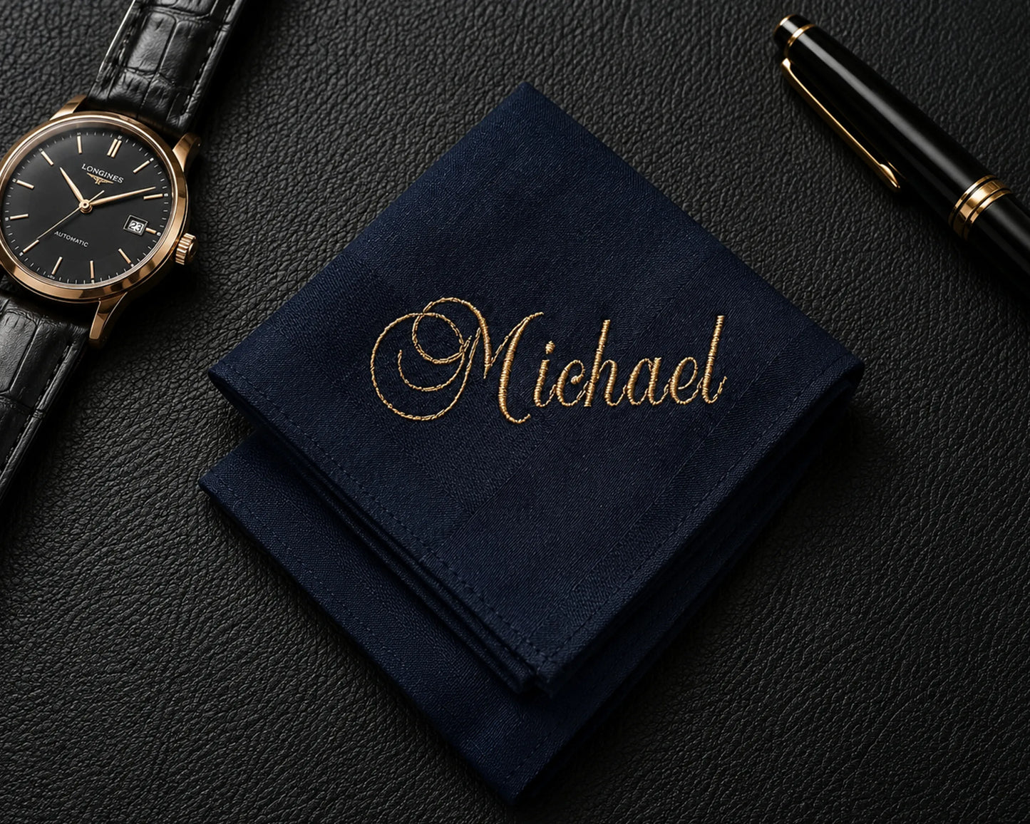 Navy blue hanky with 'Michael' embroidered on it, next to a watch and pen on a dark surface.