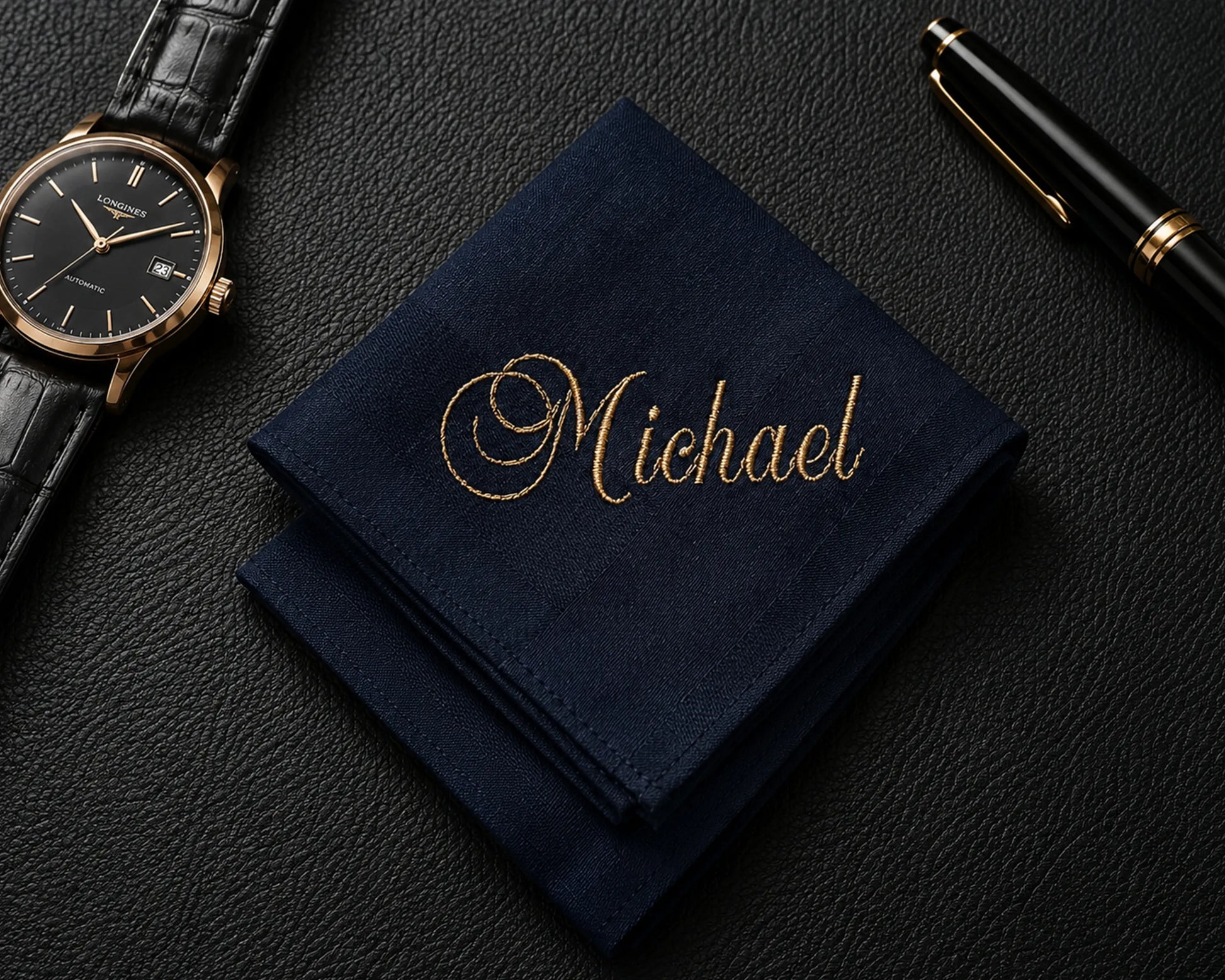 Navy blue hanky with 'Michael' embroidered on it, next to a watch and pen on a dark surface.