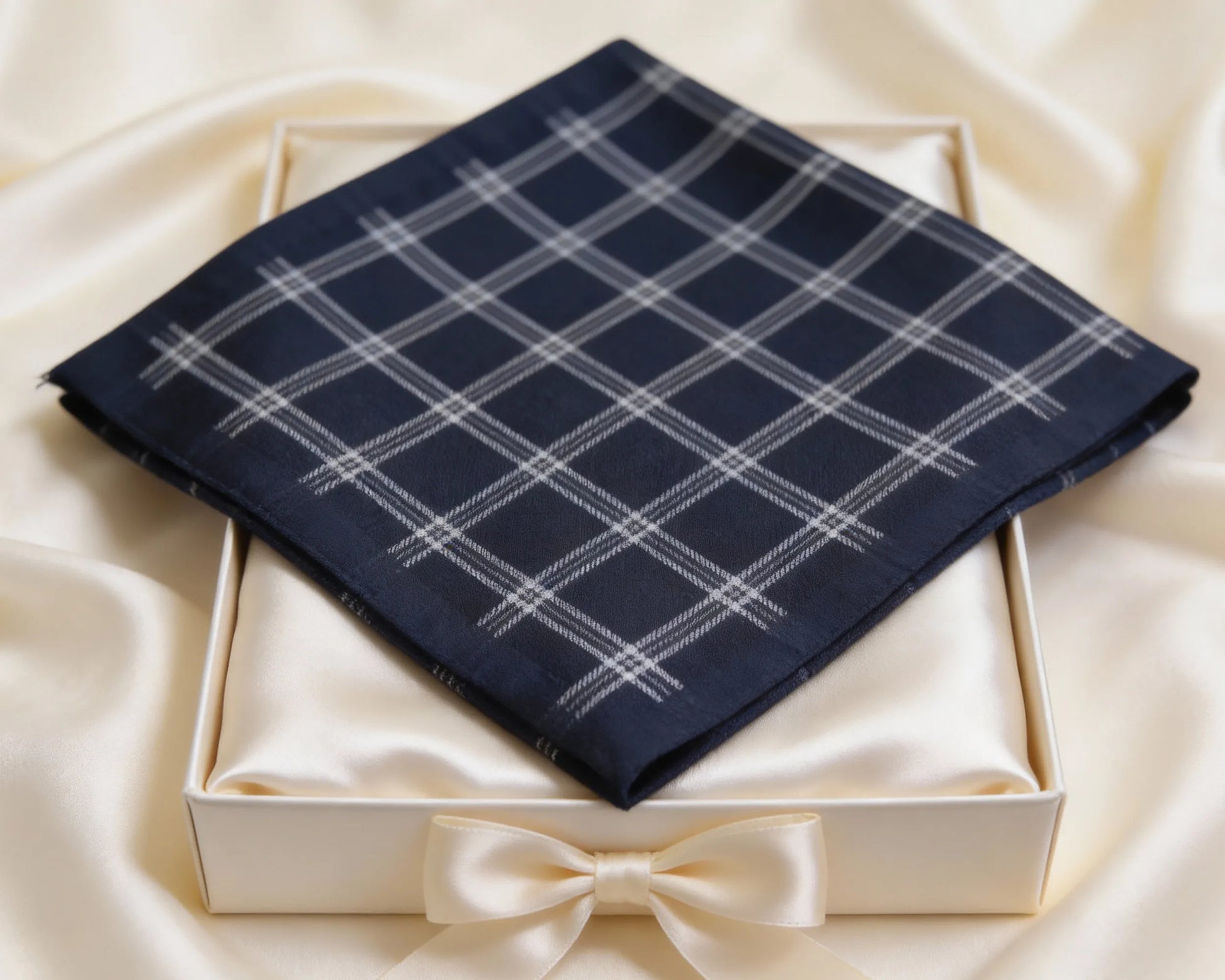 Navy plaid pocket square in a white box with a bow on a beige fabric background