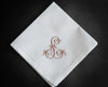 White cotton hanky with a purple embroidered circular monogram and decorative lace trim near white daisies