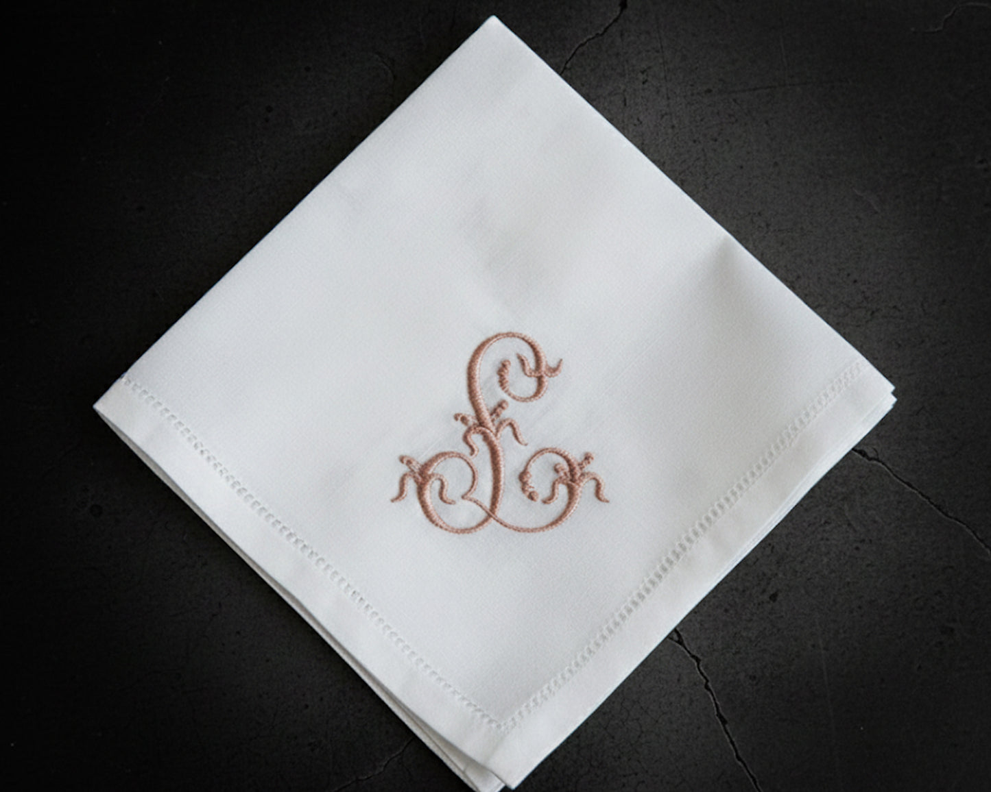 White cotton hanky with a purple embroidered circular monogram and decorative lace trim near white daisies