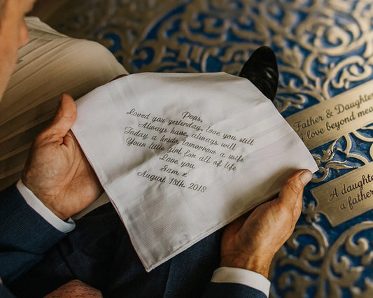 Person holding a personalized handkerchief with embroidered text against a decorative background
