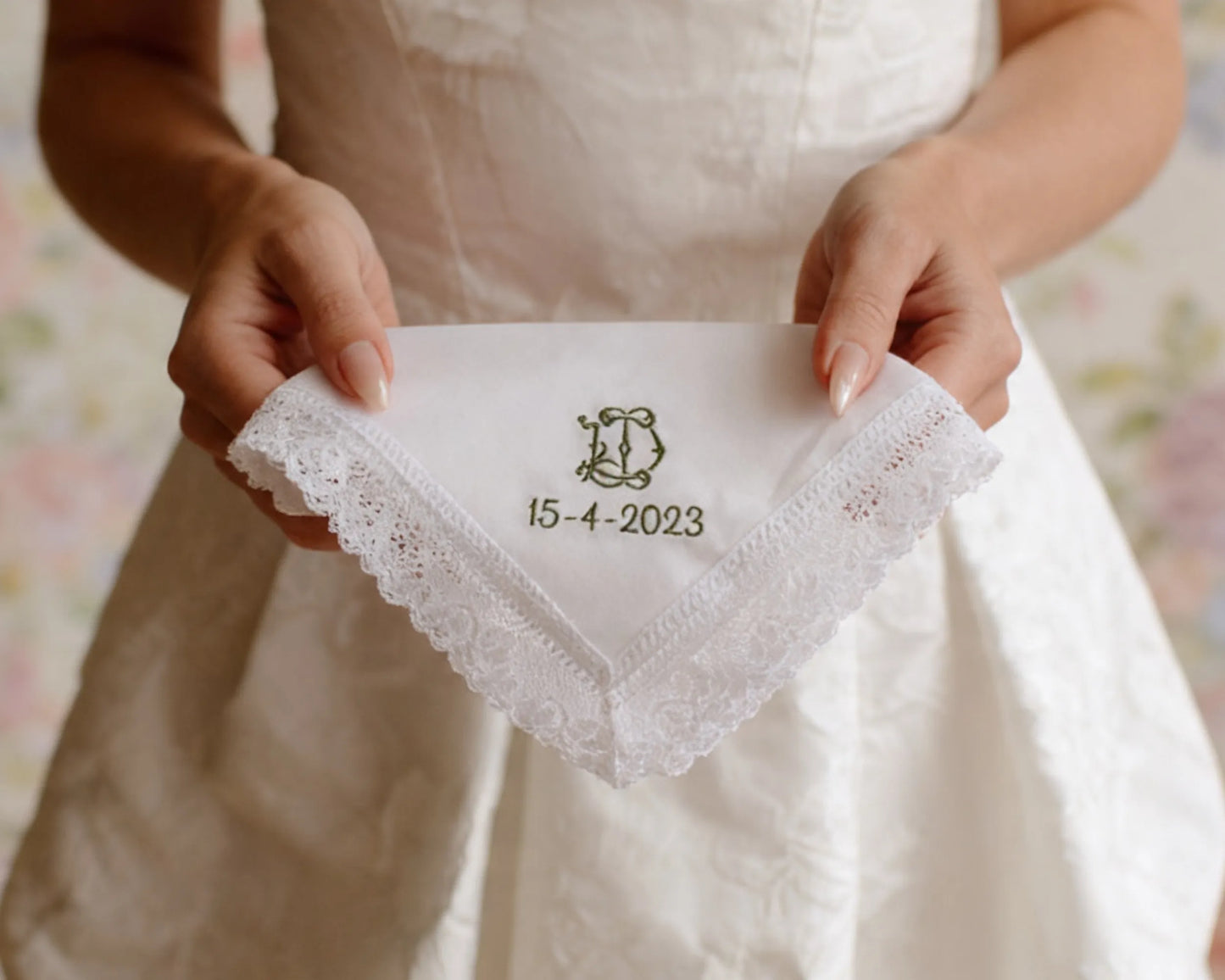 Person holding a white handkerchief with lace trim and embroidered text, wearing a wedding dress.