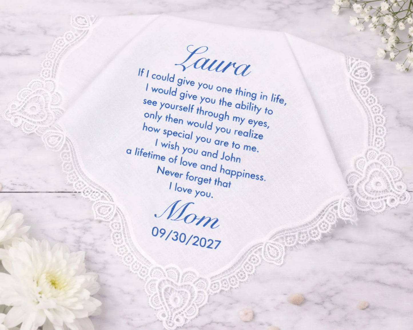 Personalized handkerchief with a message from 'Mom' to 'Laura' on a marble surface with flowers.
