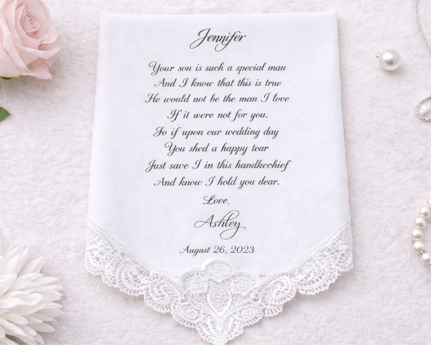 Personalized handkerchief with embroidered message on a white background with flowers and jewelry.