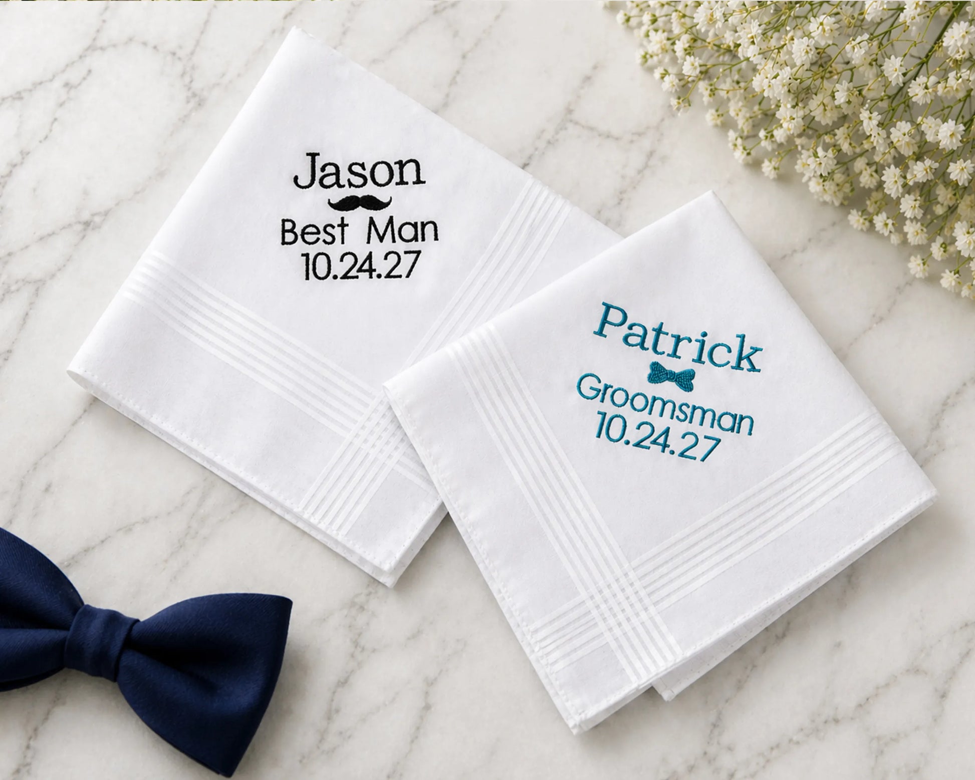 Personalized hanky for a wedding with names and dates embroided on them, placed on a marble surface with a bow tie.