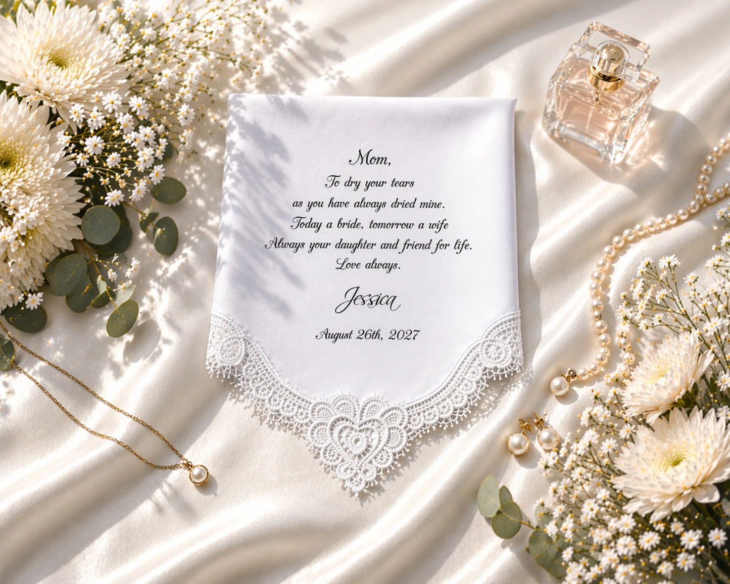 Personalized hanky with lace detailing, flowers, and jewelry on a white fabric background