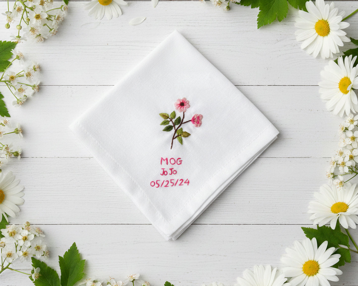 Personalized white cotton handkerchief with delicate pink floral needlework and custom red date embroidery framed by daisies