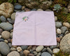 Pink embroidered fabric on a bed of stones and small plants