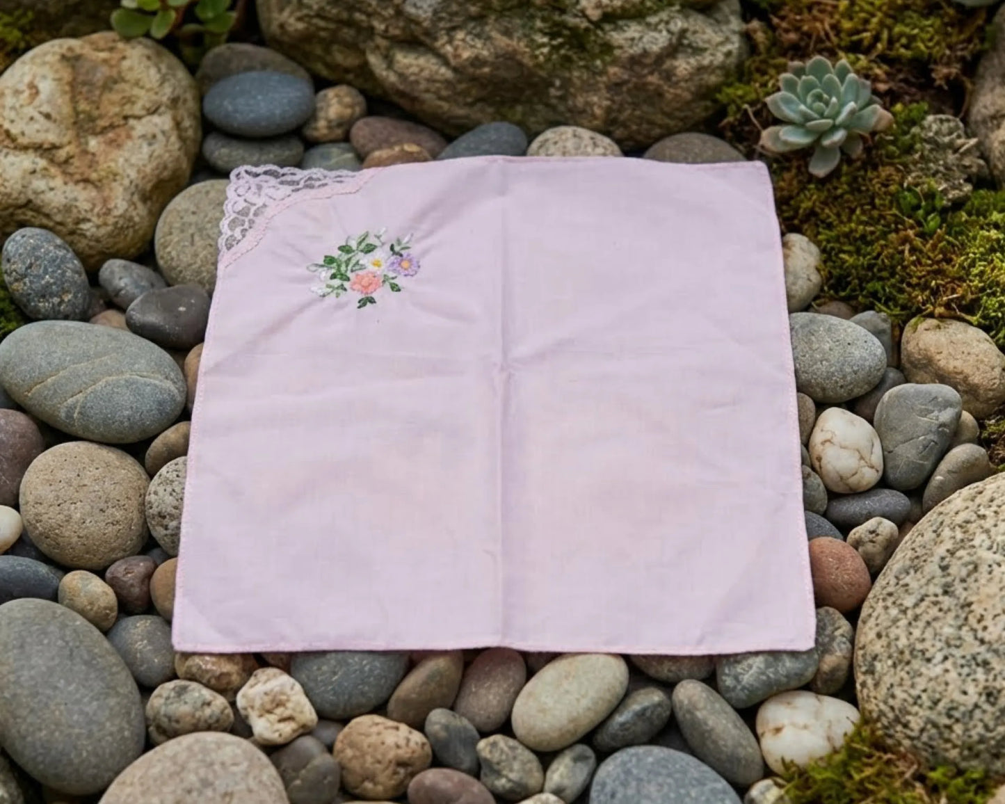 Pink embroidered fabric on a bed of stones and small plants