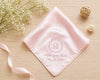 Pink handkerchief with monogram and text on a wooden surface with flowers and ribbons.