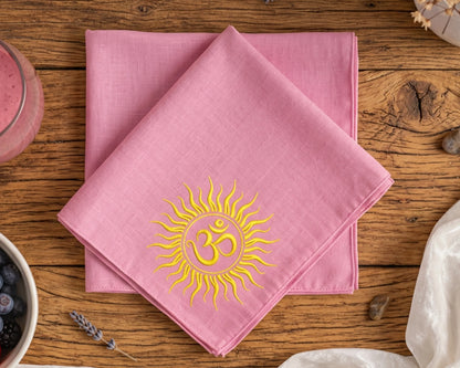 Pink hanky with a yellow sun and Om symbol on a wooden table.